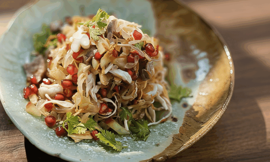 Trinarong salad with ruby pomegranate seeds, translucent pomelo segments, and golden fried shallots glistening with lime dressing on a white plate